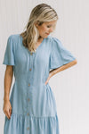 Model wearing a button up midi with a chambray color, smocked side detail and flutter short sleeves.