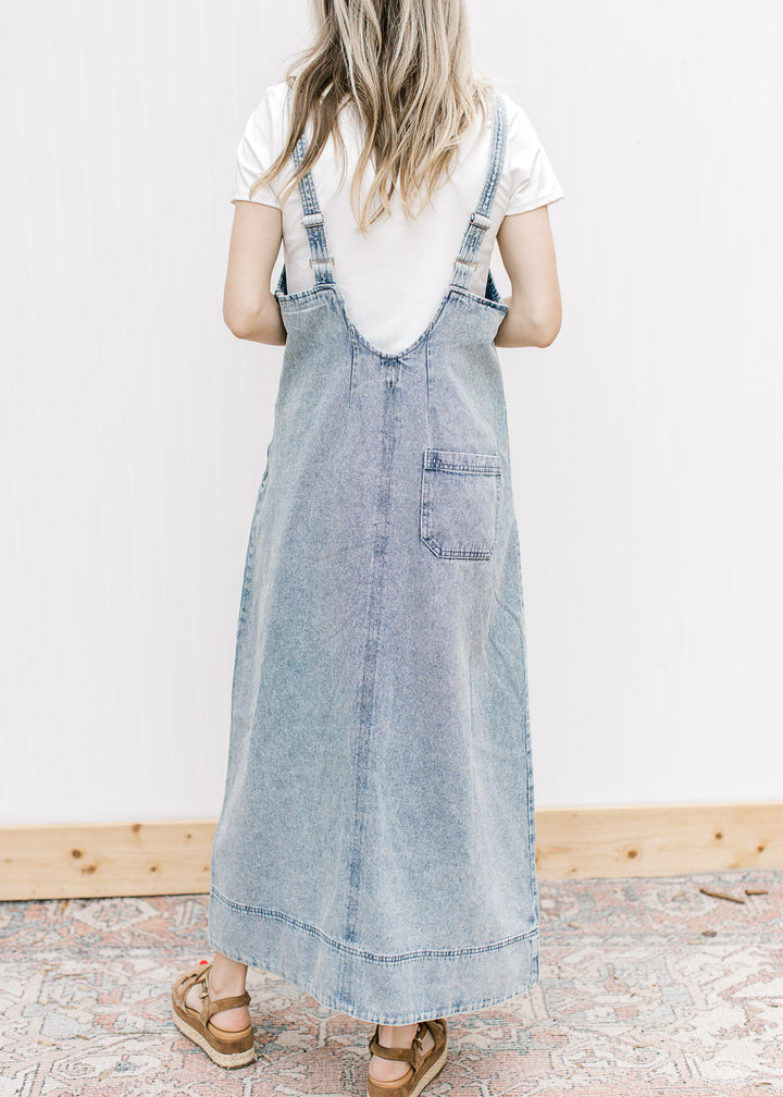 Back view of model in a light denim midi with a single pocket, adjustable straps and rounded back.