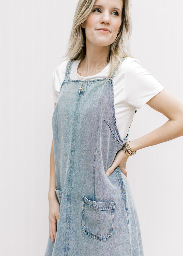 Model wearing a light denim midi with front pouch pockets, side zipper and a adjustable straps. 