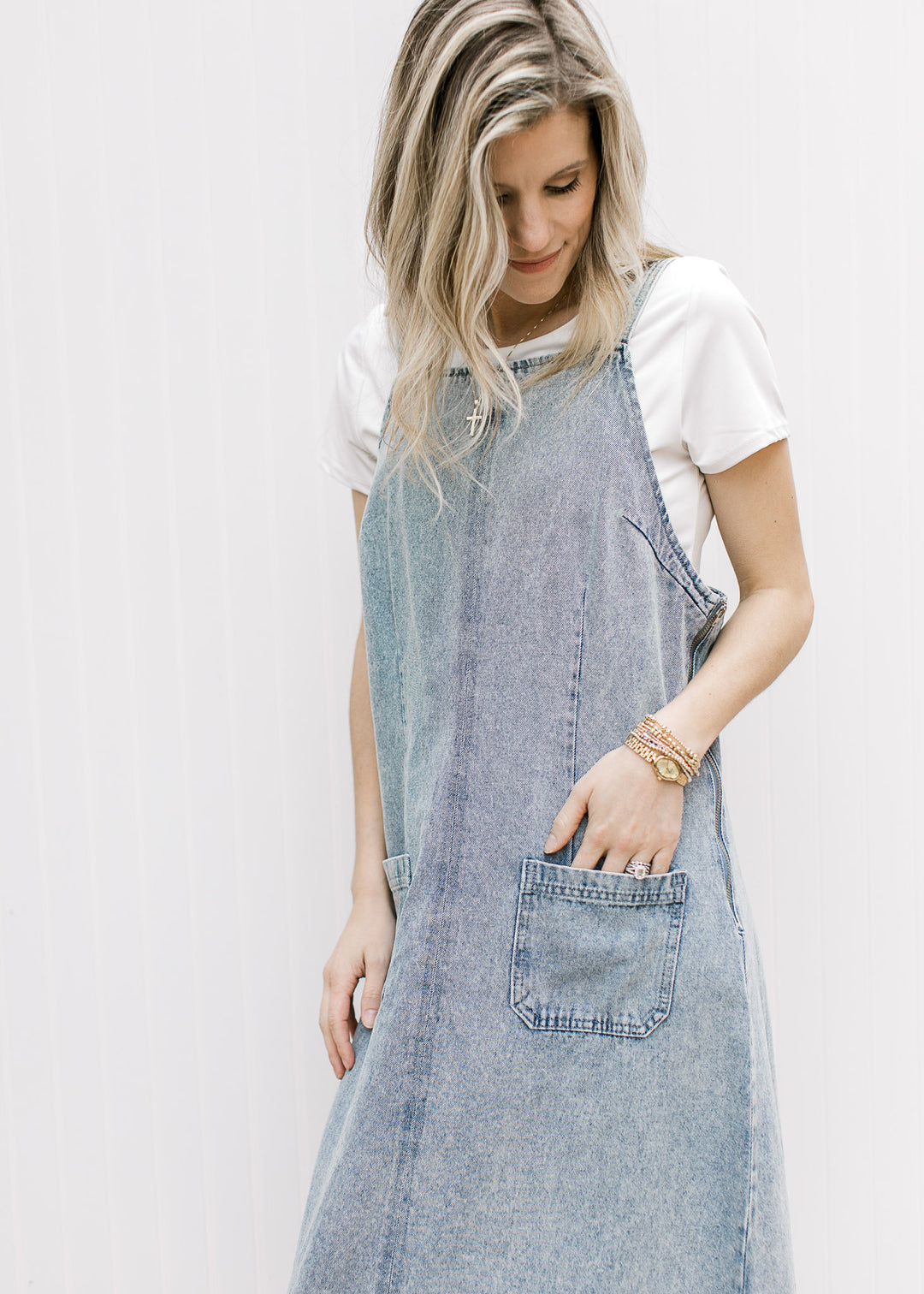Model wearing a light denim overall midi with front pouch pockets, side zipper and a rounded back. 