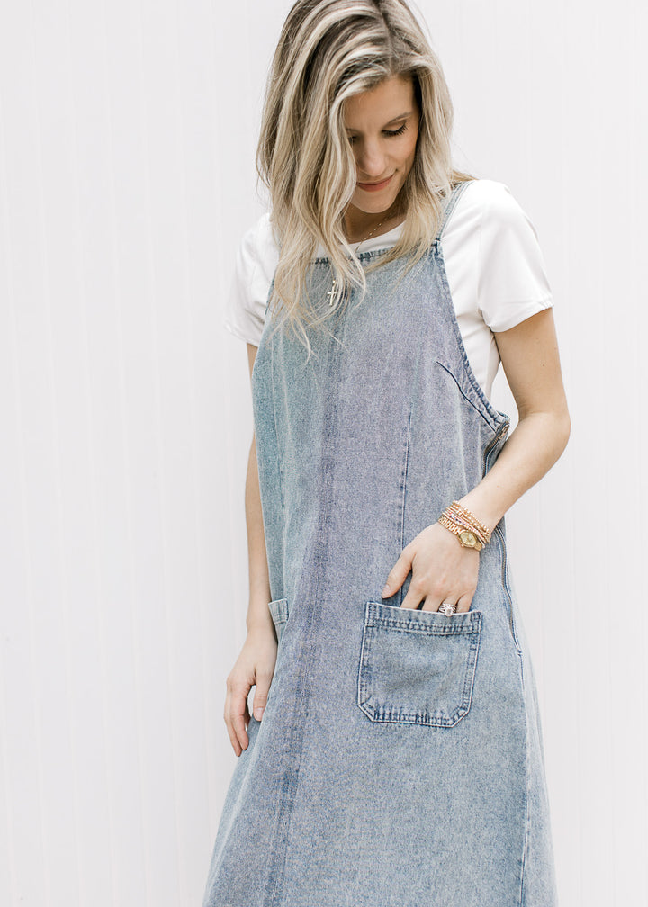 Model wearing a light denim overall midi with front pouch pockets, side zipper and a rounded back. 