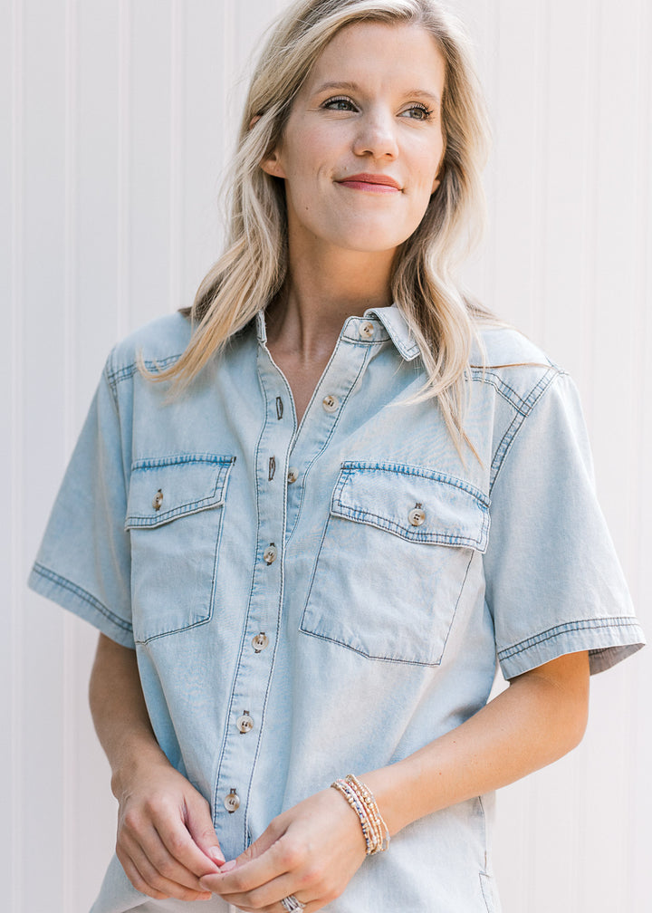 Model wearing a button up chambray top with short sleeves, traditional collar and patch pockets. 
