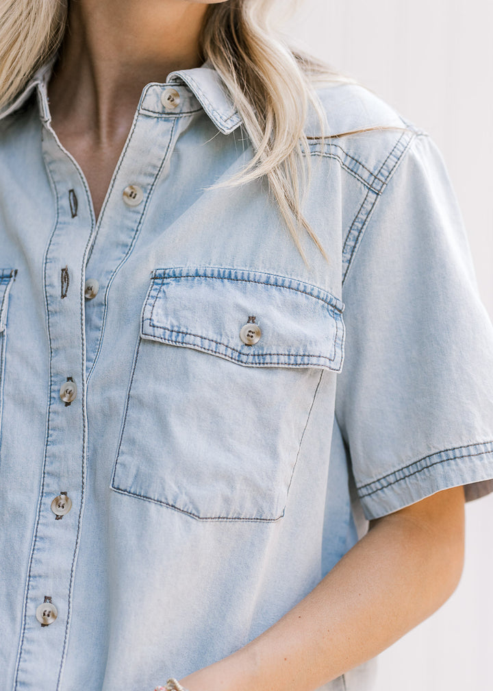 Close up of patch pockets, short sleeve and button front on a light blue chambray top. 