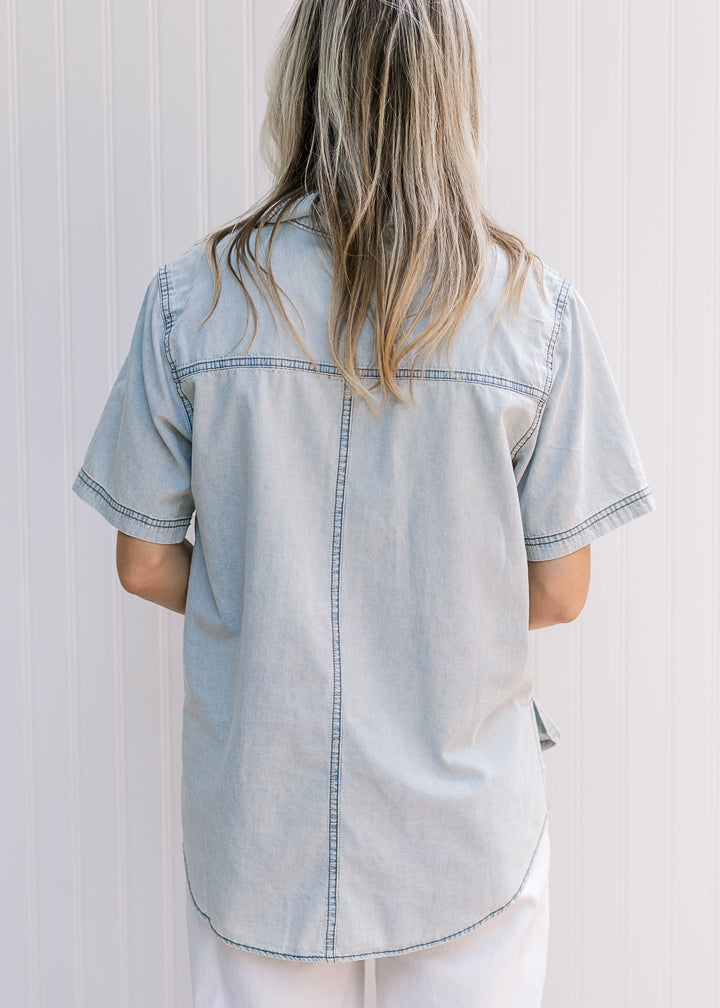Back view of Model wearing a button up chambray top with short sleeves and a traditional collar. 