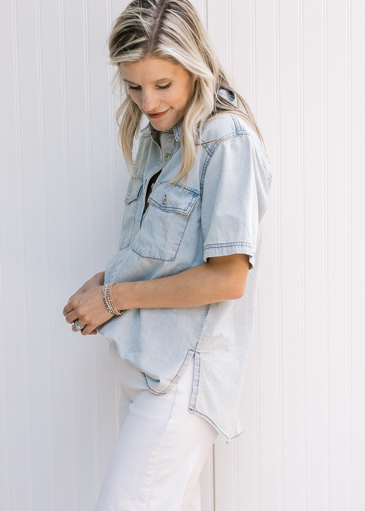 Side view of side slit on a light blue chambray button up with short sleeves and a collar. 