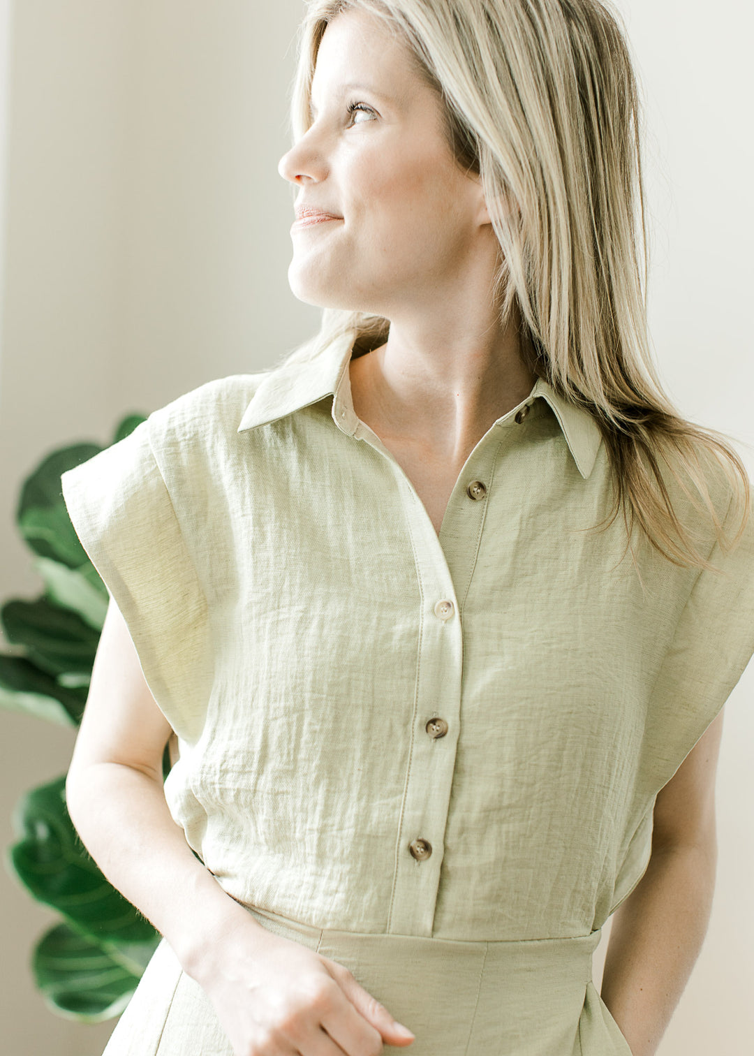 Close up of button bodice, collar and cap sleeves on a light olive midi with pockets. 