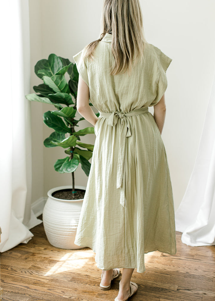 Back view of model in a light olive midi with cap sleeves, elastic waist and adjustable tie back. 