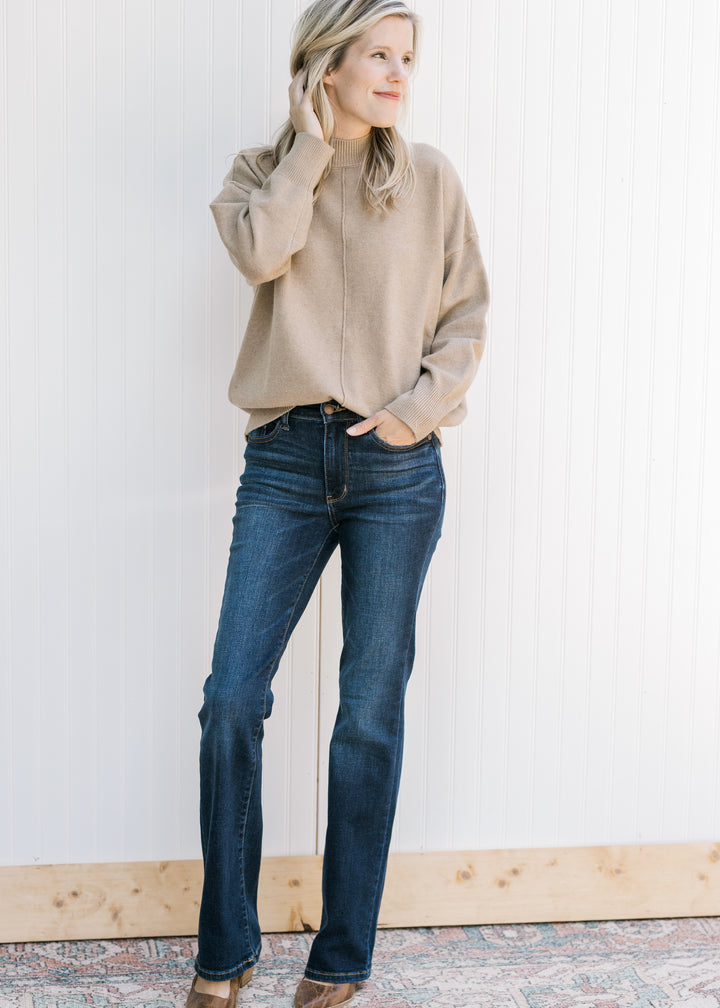 Model wearing jeans and a camel knit sweater with long sleeves and a mock neckline. 