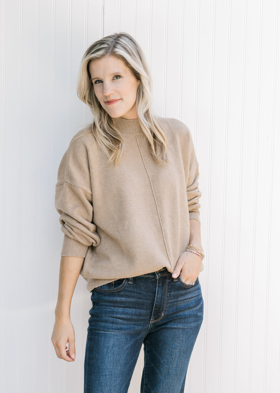 Model wearing a camel knit sweater with a seam detail down the front, mock neck and long sleeves.