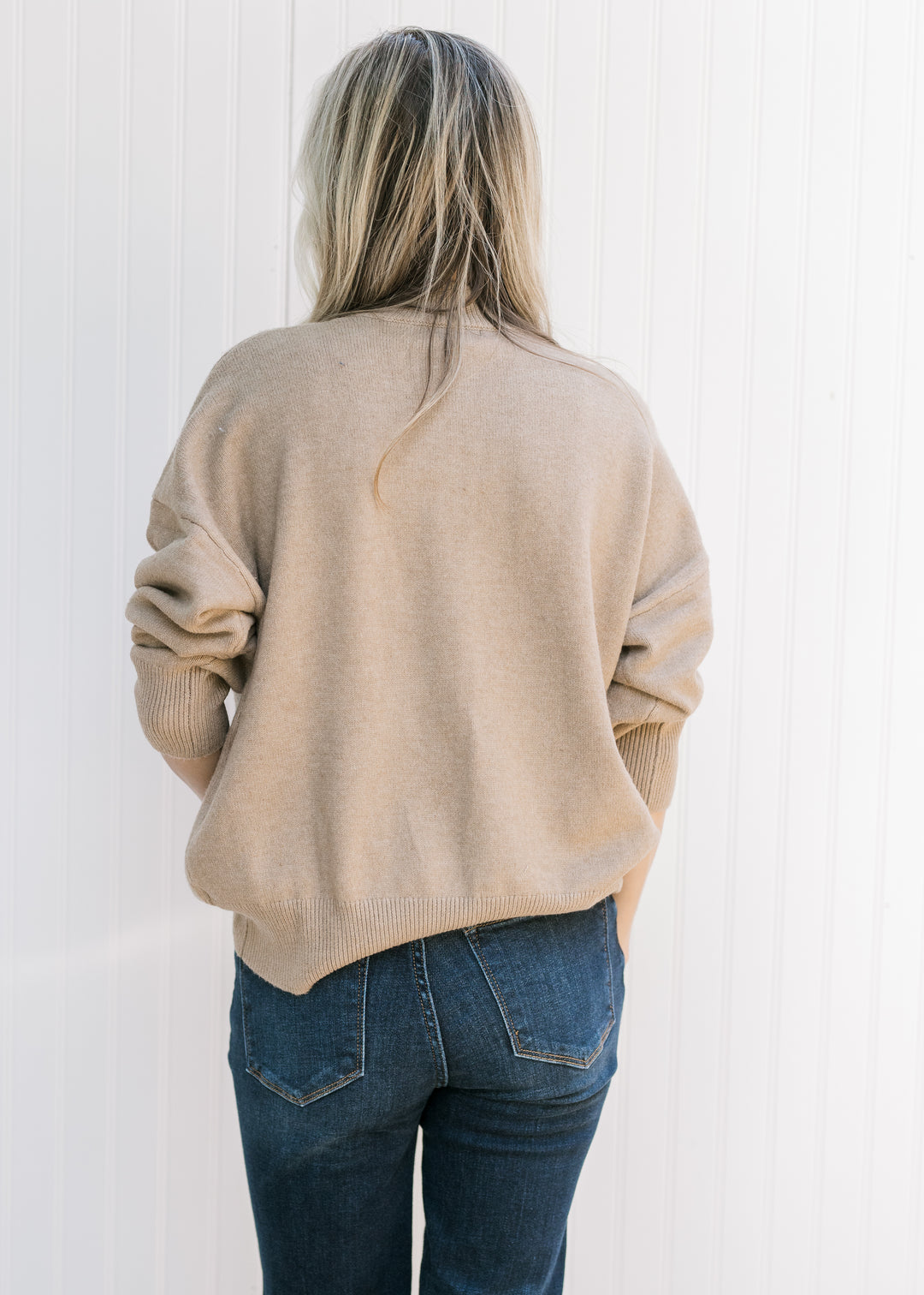 Back view of Model wearing a camel knit sweater with a mock neck and long sleeves.