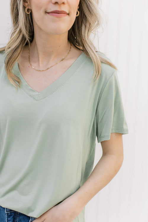 Model wearing a light sage short sleeve top with a v-neck and rayon/spandex blend. 