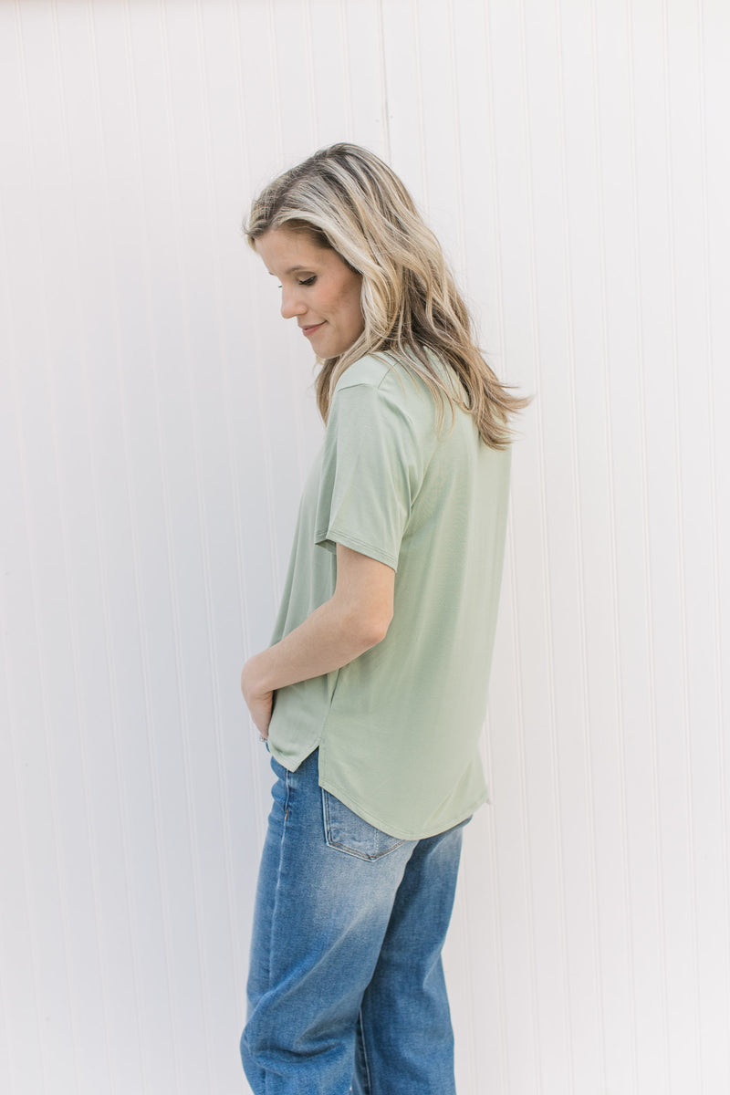 Model wearing a light sage short sleeve top with a v-neck and a small side slit.