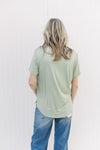 Back view of Model wearing a light sage short sleeve top with a v-neck and rayon/spandex blend.