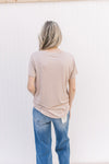 Back view of Model wearing a light taupe short sleeve top with a v-neck and rayon/spandex blend.