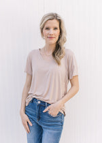 Model wearing jeans with  a light taupe short sleeve top with a v-neck and rayon/spandex blend.