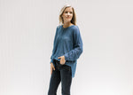 Model wearing a deep blue sweater with exposed hem, long sleeves, and ribbing at the hem and cuff.