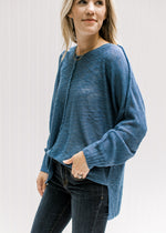 Model wearing jeans with a deep blue sweater with exposed hem, and ribbing at hem and cuff. 