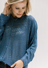 Close up of exposed hem on a deep blue sweater with ribbing at the hem and cuffs. 