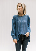 Model wearing a deep blue lightweight knit sweater with exposed hem and long sleeves. 