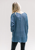 Back view of Model wearing jeans and booties with a deep blue lightweight sweater with exposed hem. 