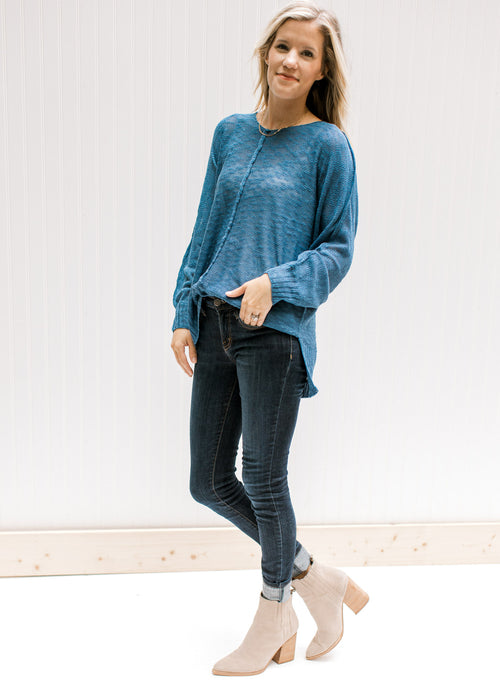 Model wearing jeans and booties with a deep blue lightweight sweater with exposed hem. 