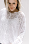 Model wearing a semi-sheer cream loose knit sweater with long sleeves and exposed hem. 