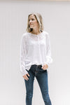Model wearing jeans with a semi-sheer cream loose knit sweater with long sleeves and exposed hem. 