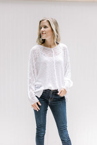 Model wearing jeans with a semi-sheer cream loose knit sweater with long sleeves and exposed hem. 