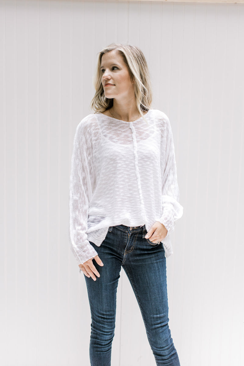 Model wearing jeans with a semi-sheer cream loose knit sweater with long sleeves and exposed hem. 
