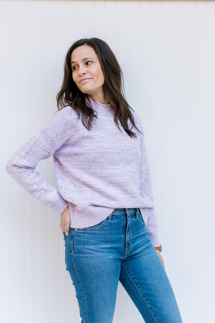 Model wearing jeans with a lilac long sleeve sweater with a mock neckline and a ribbed cuff and hem.