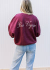 Back view of Model wearing a maroon sweatshirt with a cream emblem, long sleeves and fleece lining. 