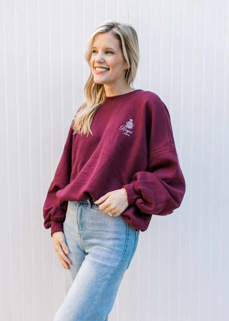 Model wearing jeans and a maroon sweatshirt with a cream emblem, long sleeves and fleece lining. 