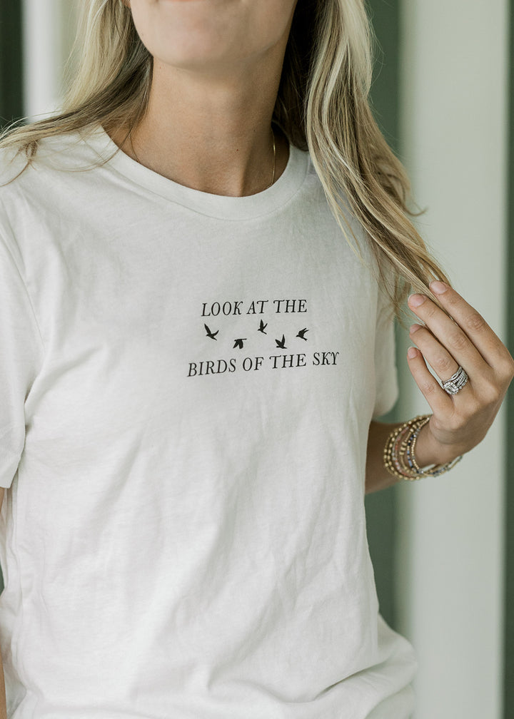 Model wearing a cream tee with a crew neck and black look at the birds of the sky graphic.
