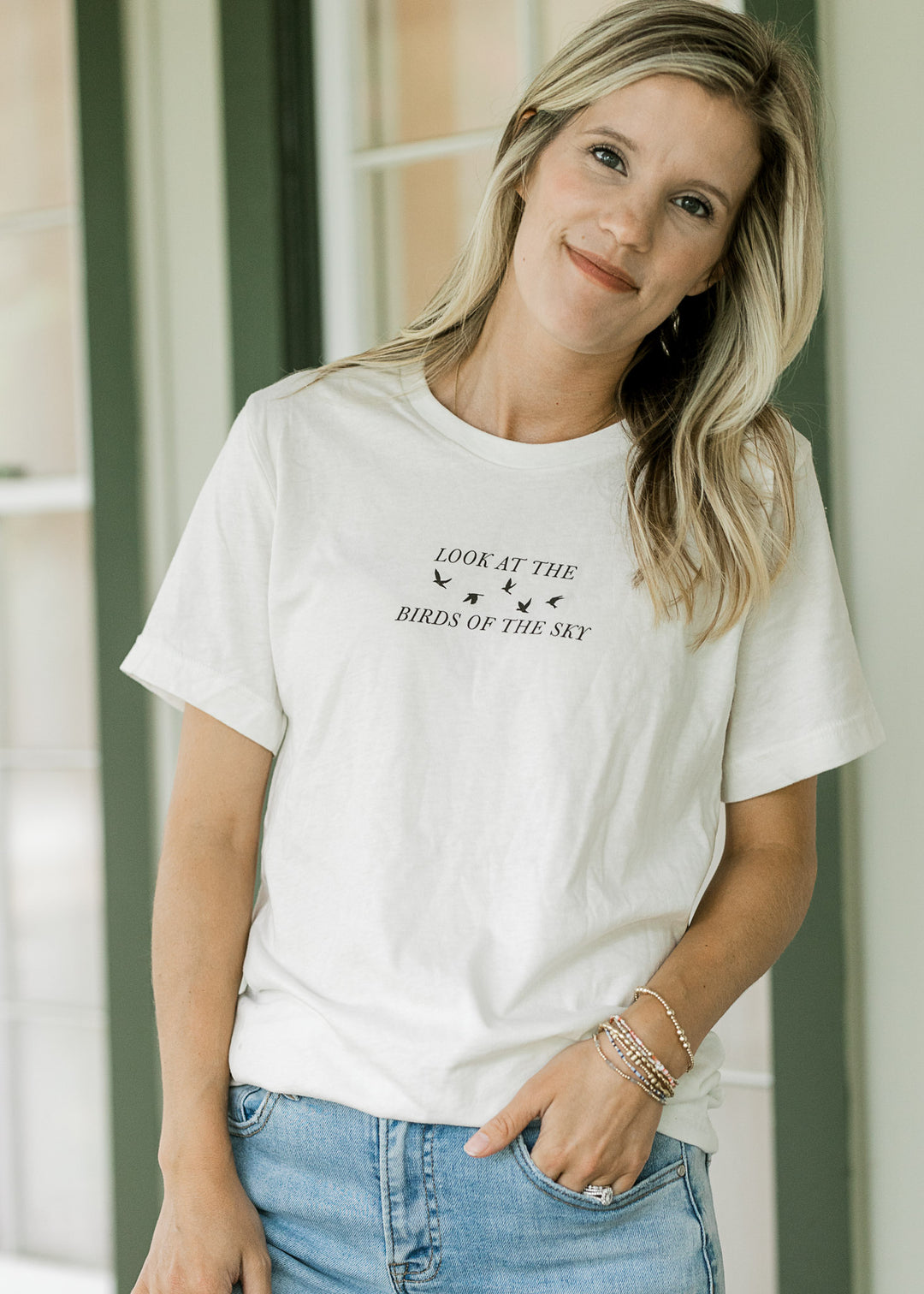 Model wearing a cream top with a crew neck and black look at the birds of the sky graphic.