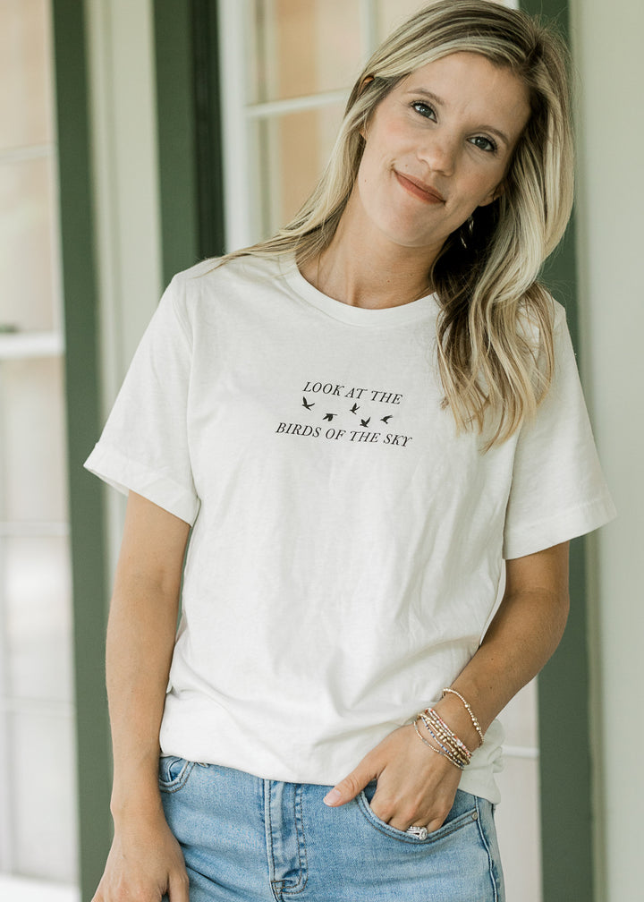 Model wearing a cream top with a crew neck and black look at the birds of the sky graphic.