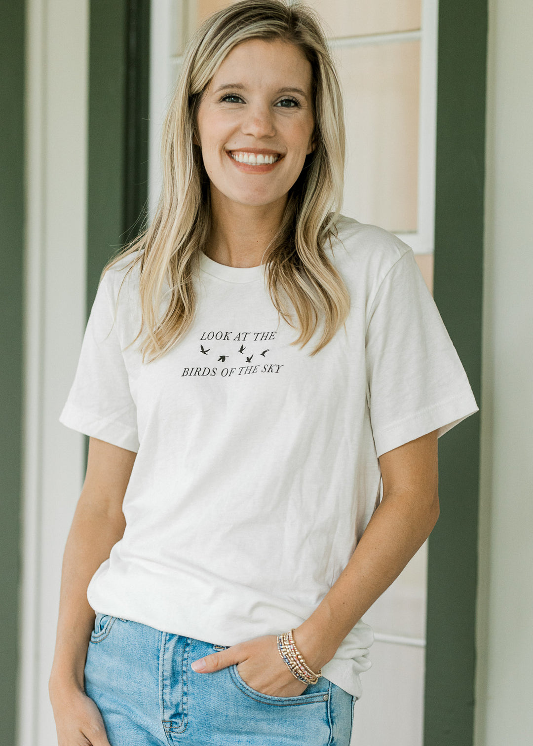 Model wearing jeans and a cream tee with a crew neck and black look at the birds of the sky graphic.
