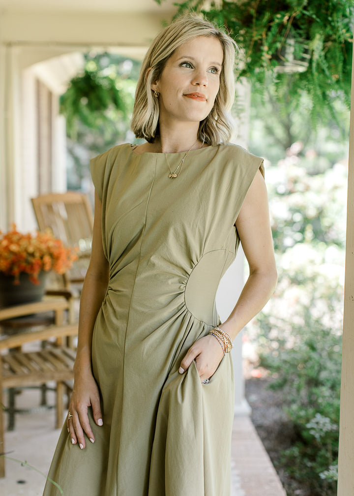Close up of Model wearing a mossy tan sleeveless maxi with pockets and ruched side panels. 