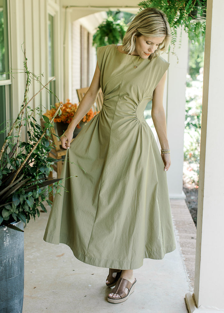 Model wearing wedges and a mossy tan maxi with hidden zipper and ruched side panels at the waist. 