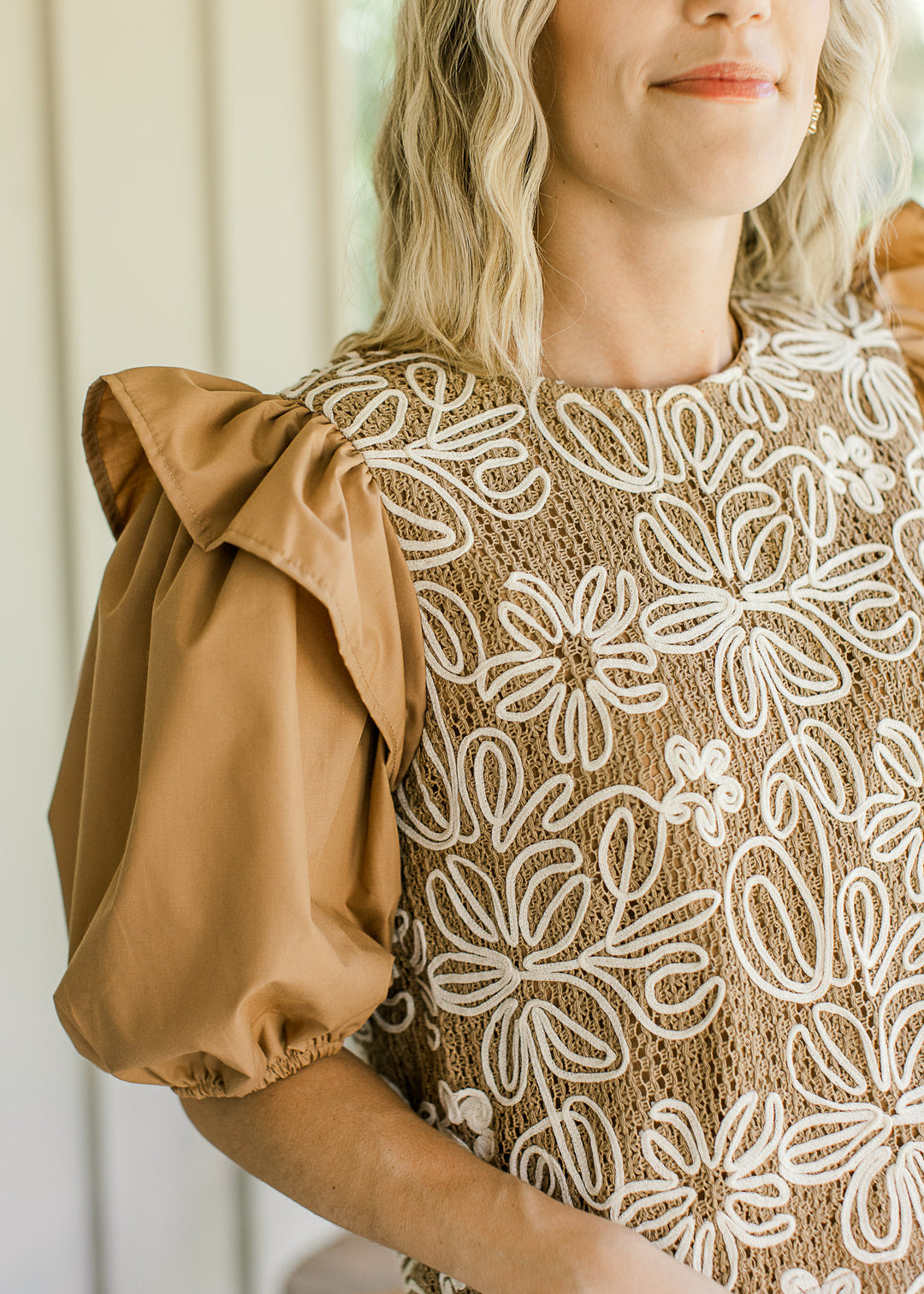 Close up of ruffle at shoulder of short puff sleeves on a camel top with white flowers. 