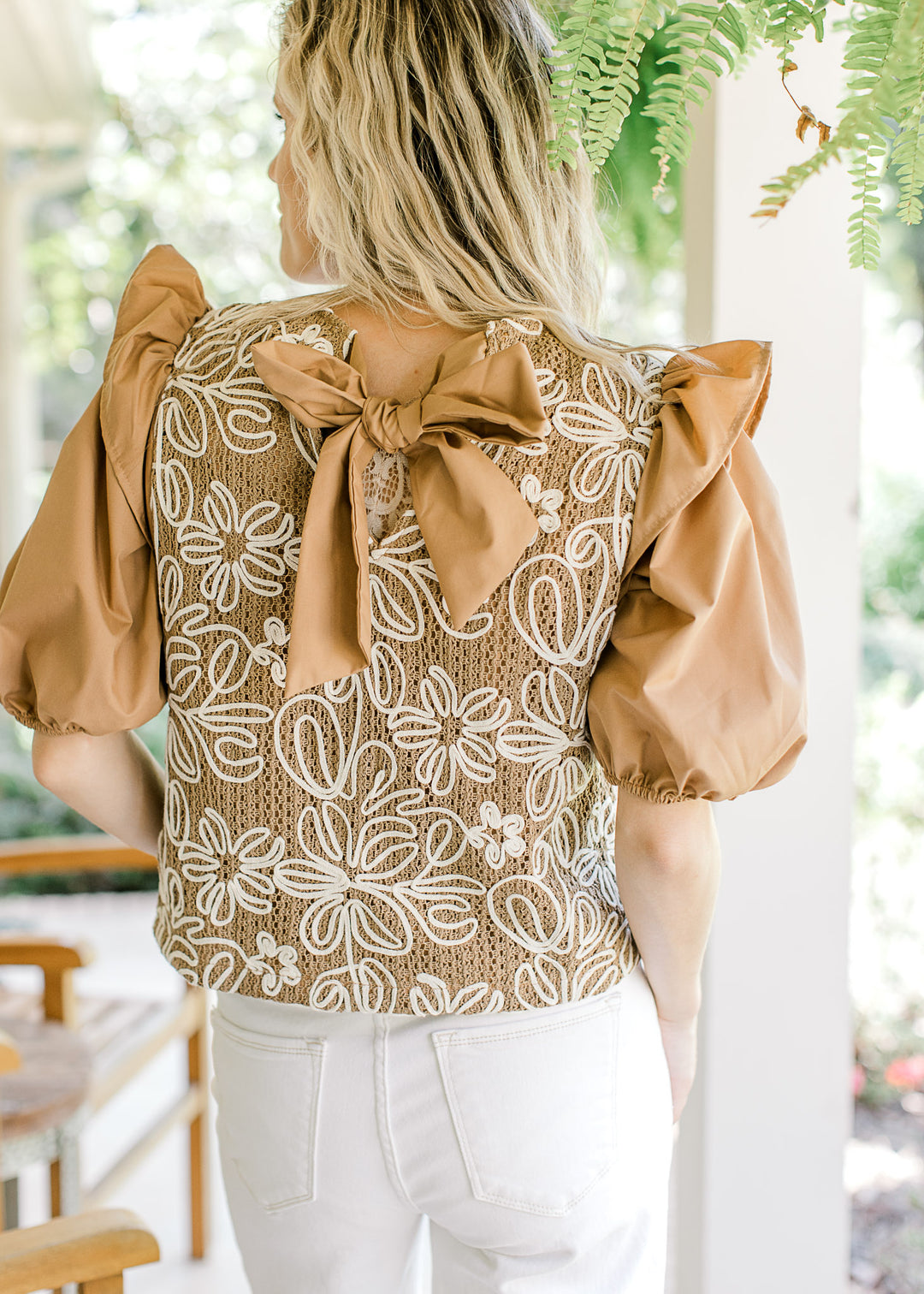 Back view of tie closure on a camel top with white flowers and short puff sleeves. 
