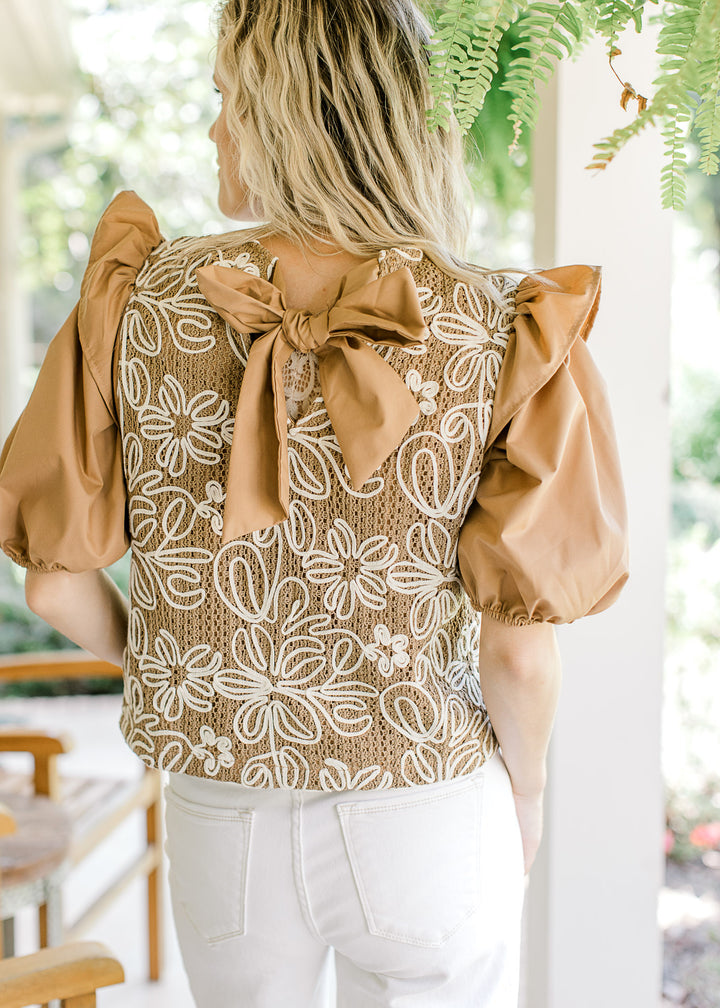 Back view of tie closure on a camel top with white flowers and short puff sleeves. 