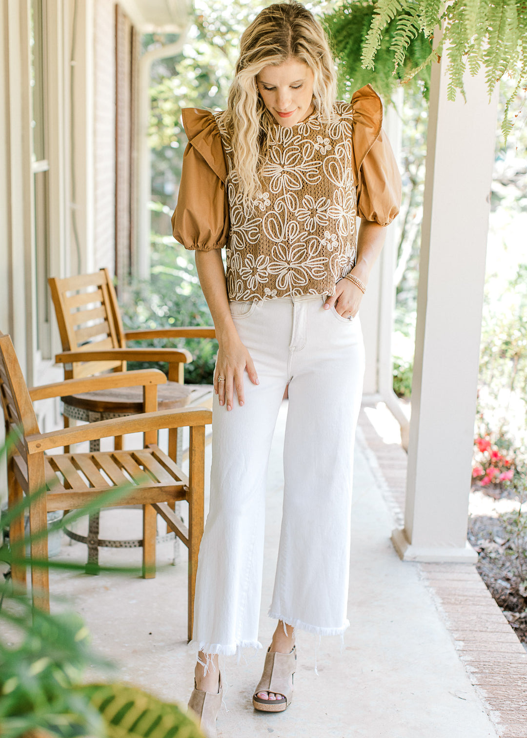 Model wearing white pants and camel top with white flowers and short puff sleeves. 
