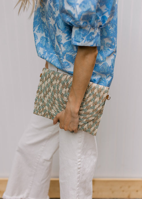 Model holding a gold, taupe, cream, and teal color lined purse with a snap closure. 
