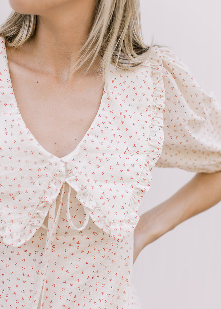 Close up of exaggerated flap collar with ruffle and tie detail on a cream dress with rose floral.