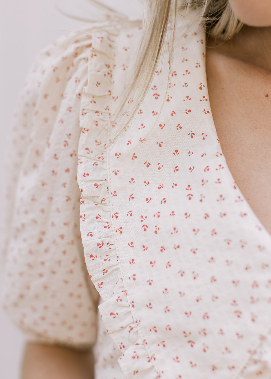 Close up of pleated shoulders and ruffle on collar of a cream dress with ditsy rose floral.