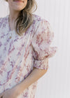 Close up of pleated shoulder and elastic band on the short sleeve of a cream top with mauve floral. 