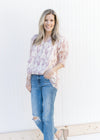 Model wearing a cream top with a mauve floral pattern, short sleeves and a v-neck.