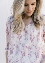 Close up of v-neck on a model wearing a cream top with a mauve floral design and short sleeves. 