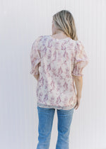 Back view of Model wearing a cream top with a mauve floral pattern, short sleeves and a v-neck.
