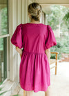 Back view of Model wearing a magenta dress with short puff sleeves and bow tie front closure. 